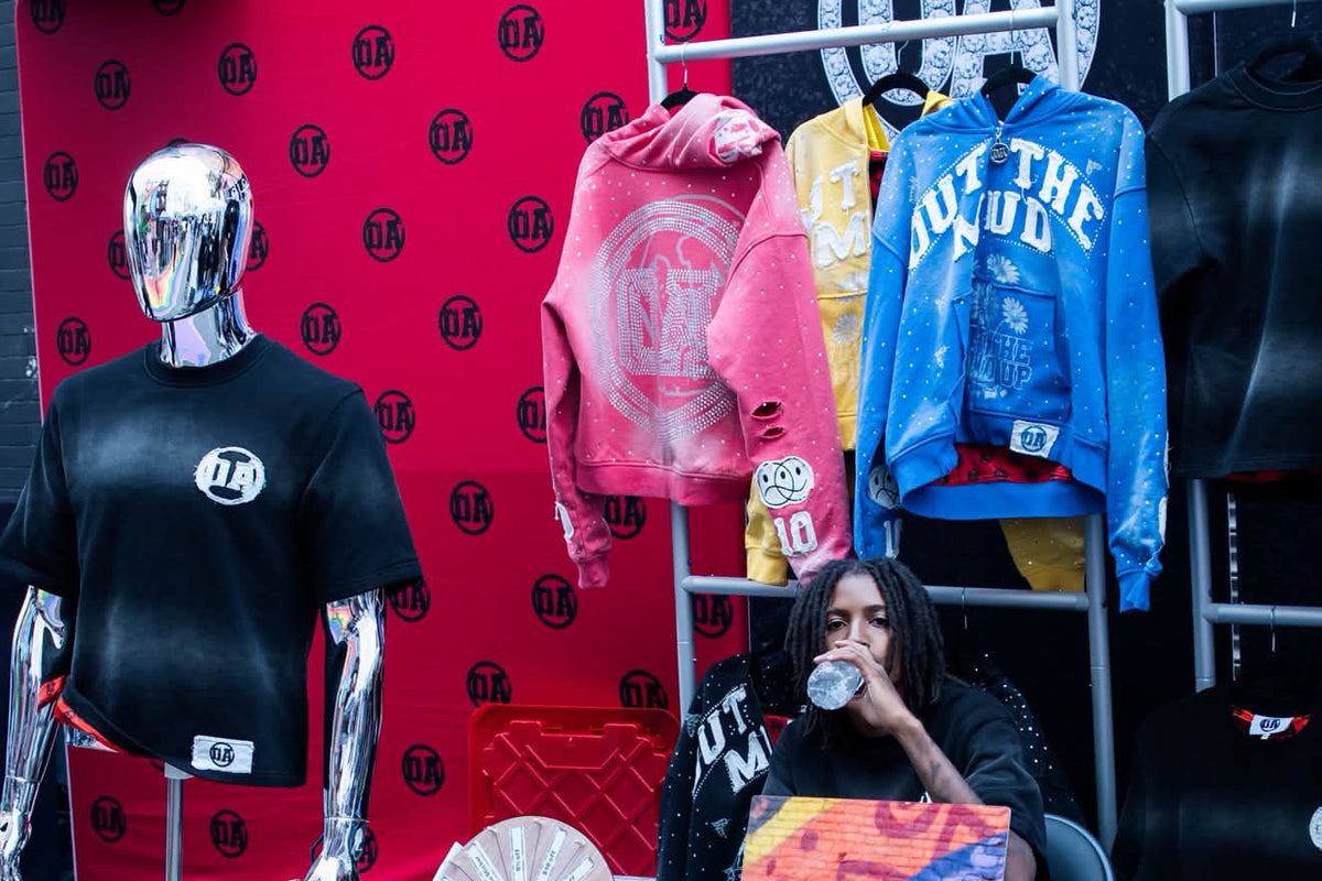 The OA pop-up booth with the Origin Blank tee on a chrome mannequin and the OUT THE MUD rack
