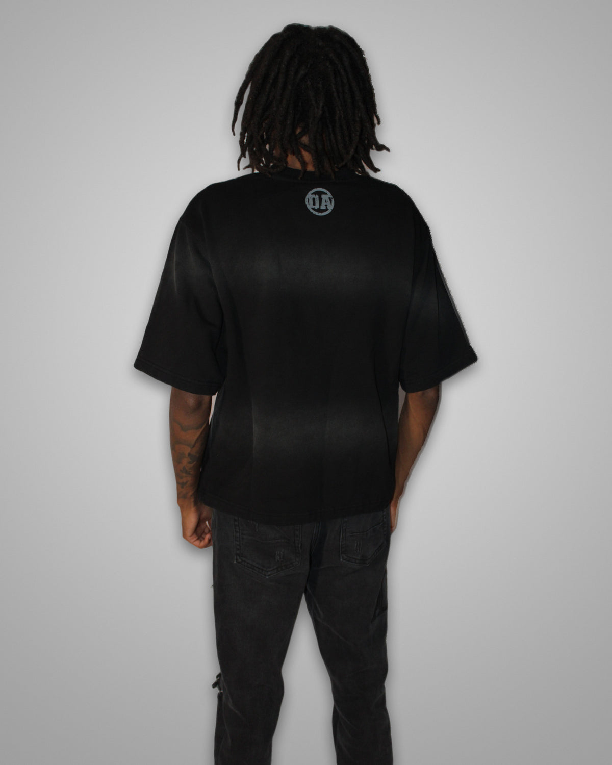 Origin Blank tee in black worn from the back, OA circle print at the neck, boxy fit